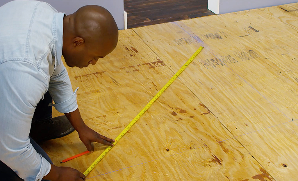 Man uses a measuring tape to measure subfloor for carpet tile installation.