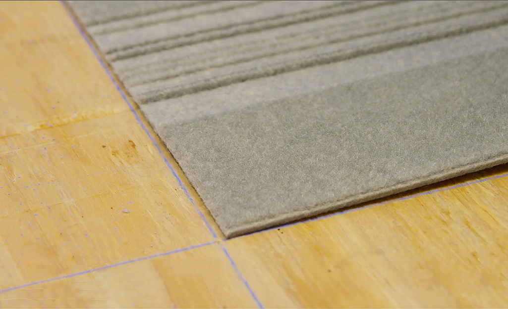 A center carpet tile is placed with its edges along marked guidelines on the floor.