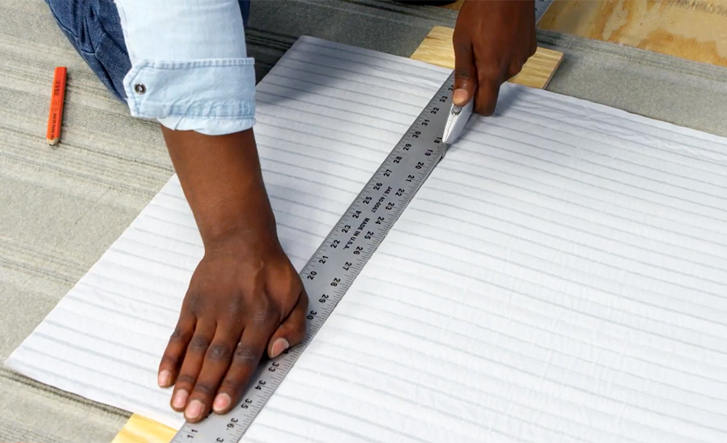 Man trims carpet tile using a utility knife and a straight edge ruler.