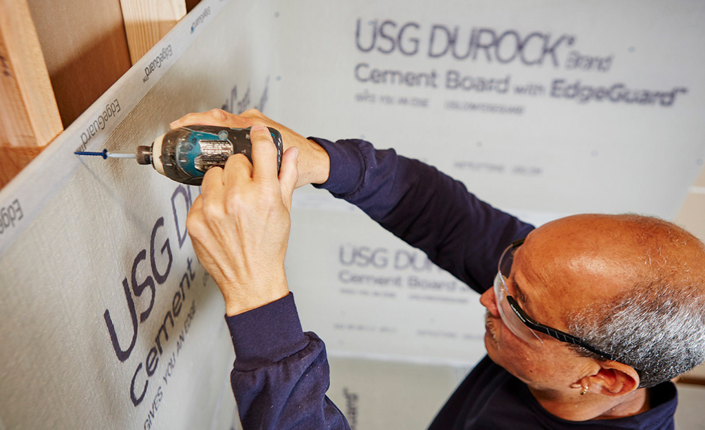 A man installs cement board on a shower wall.