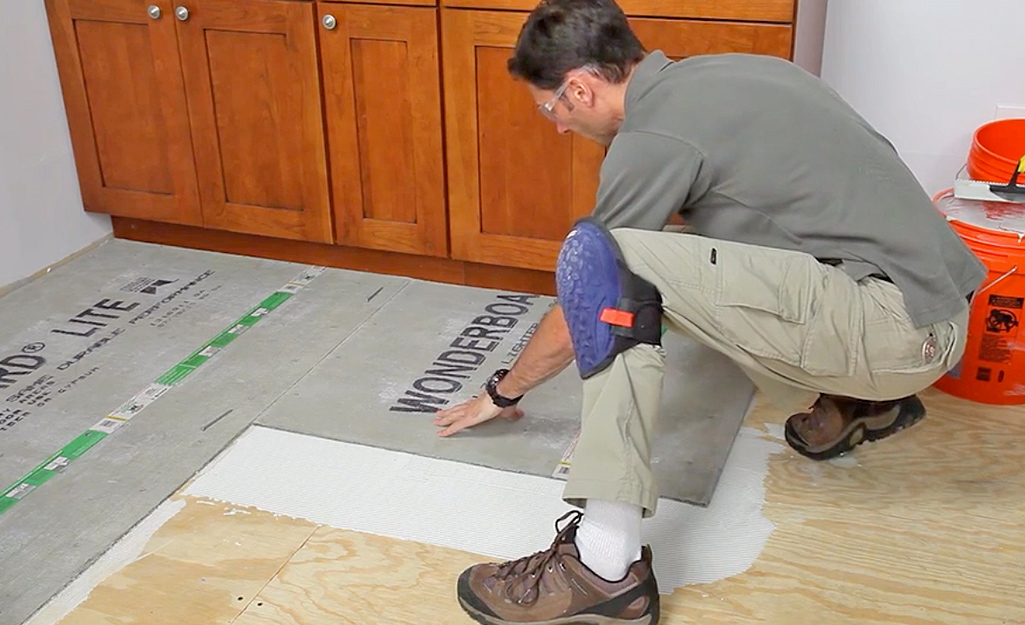 A man lays cement backerboard sheets over mortar.