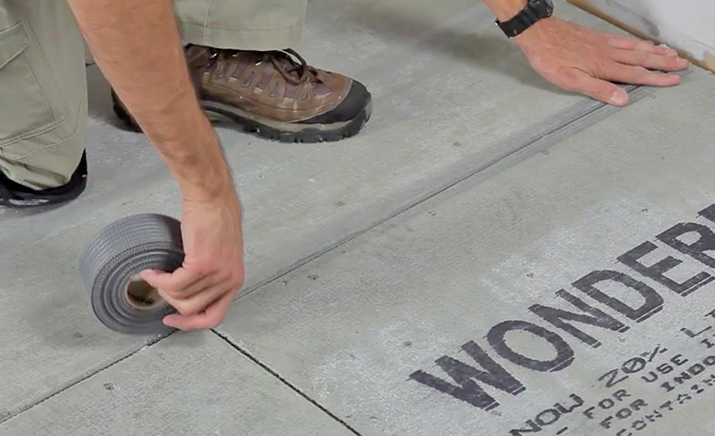 A person covers backerboard joints with fiberglass tape.