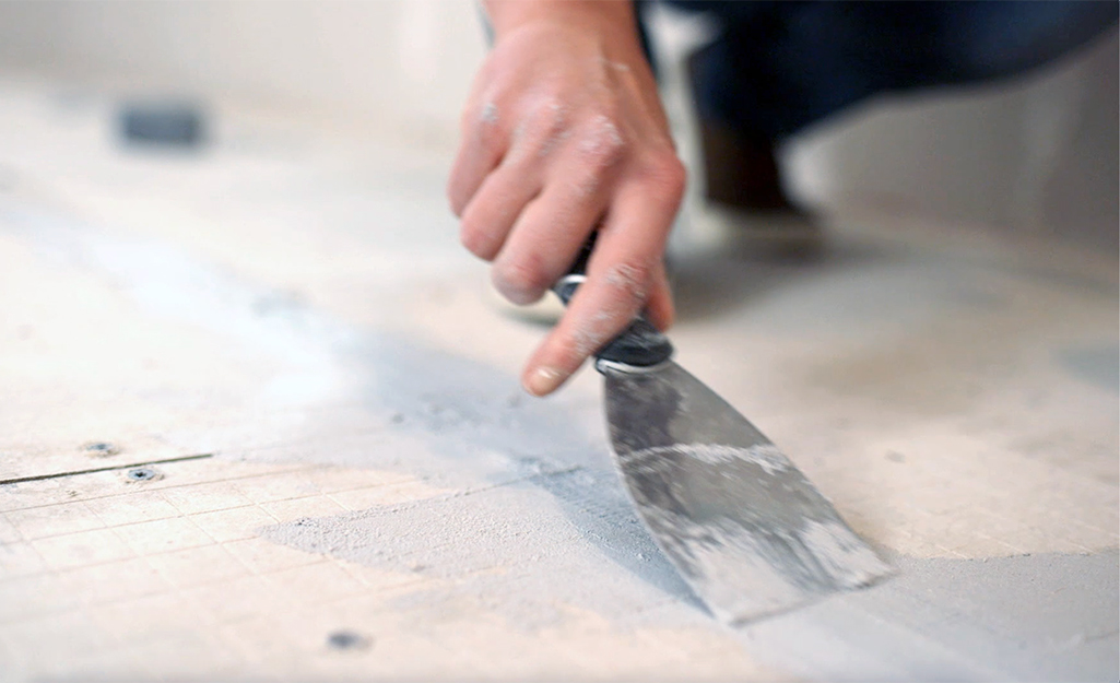 A person covers fiberglass tape with mortar.