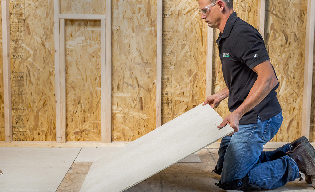 A man installs cement backerboard.