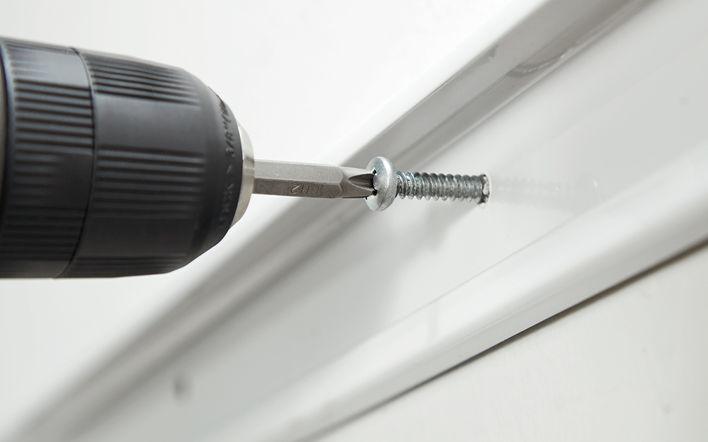 A person drills a toggle bolt into the wall to secure a hang track.