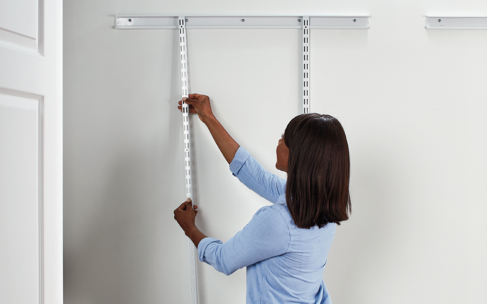 A woman attaches ClosetMaid ShelfTrack standards to the hang track.