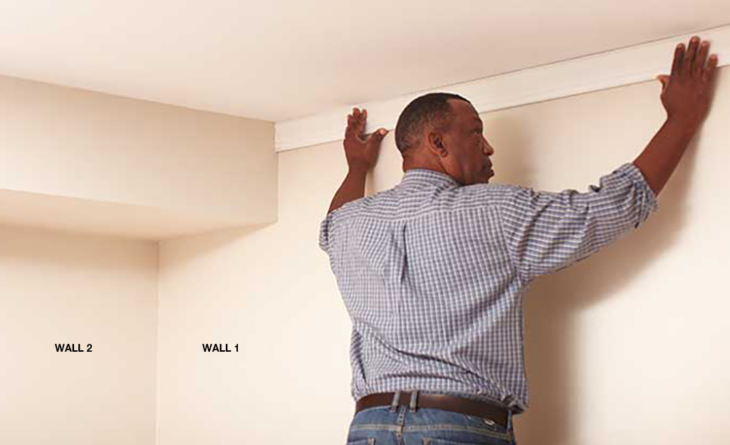 Person installing a piece of crown moulding flush with the wall and ceiling. 