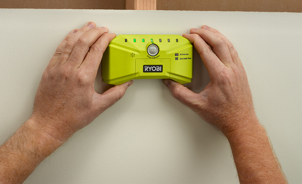 Someone using a stud finder on a wall.