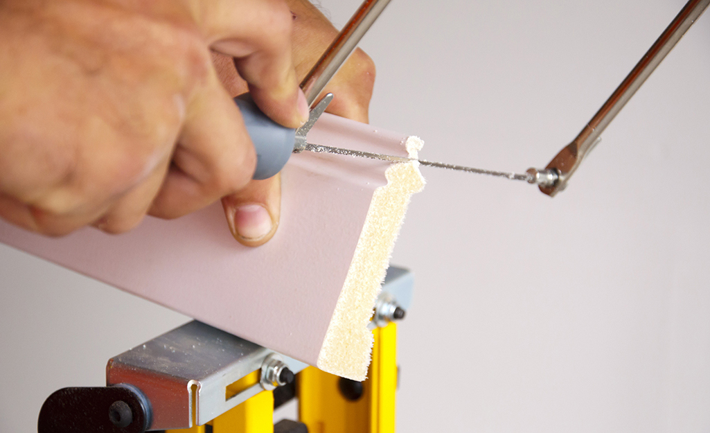 Person using a coping saw to undercut along the profile of a piece of crown moulding 