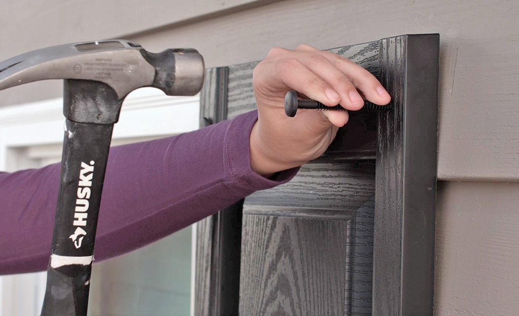 A hammer taps a shutter fastener to install an exterior shutter.
