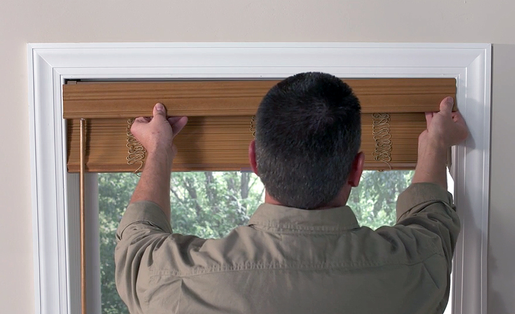 A man hangs the valance clip for his faux wood blinds.