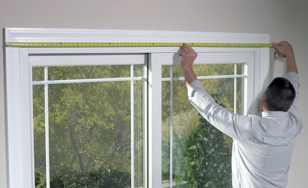 A man measures the width of a window before installing blinds.