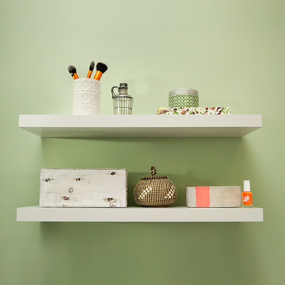 Two white floating shelves on a green wall.