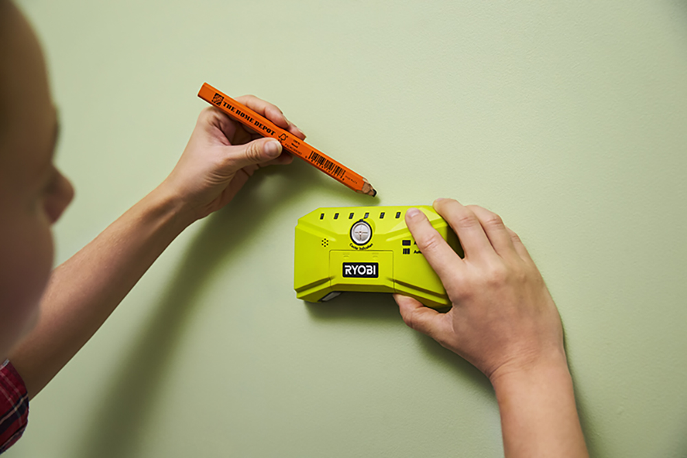 A person using a stud finder and pencil to locate the stud in a wall. 