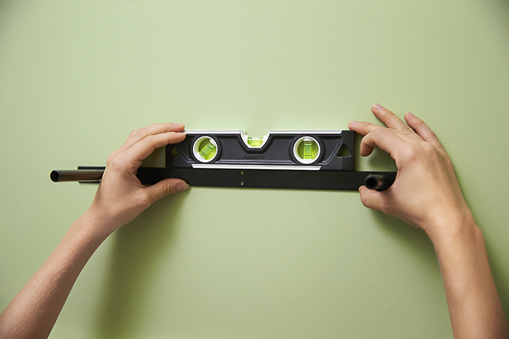 A person holding a shelf bracket and level against a wall.