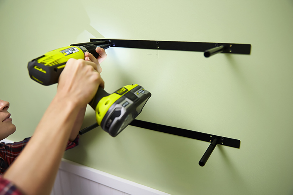 A person installs a shelf bracket to a wall using a cordless drill.