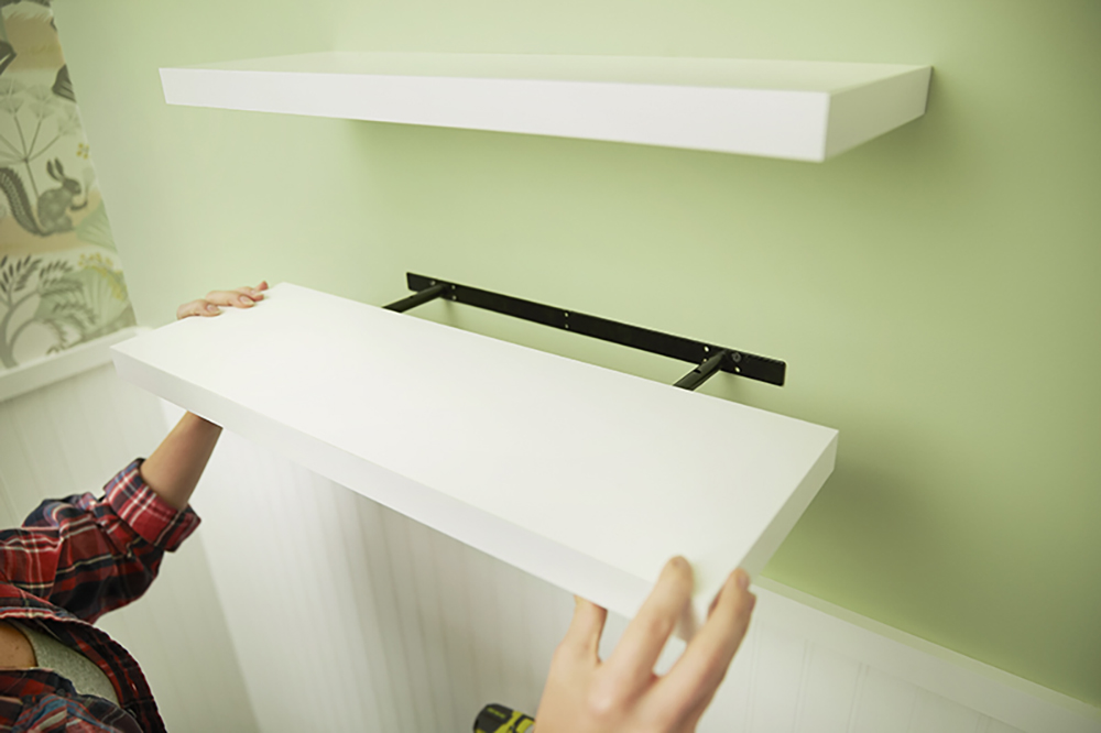 A person adding a white shelf casing to an install shelf bracket.