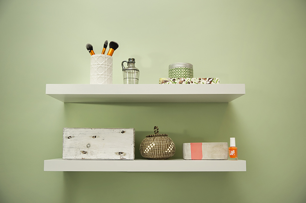 Two decorated white floating shelves on a green wall.