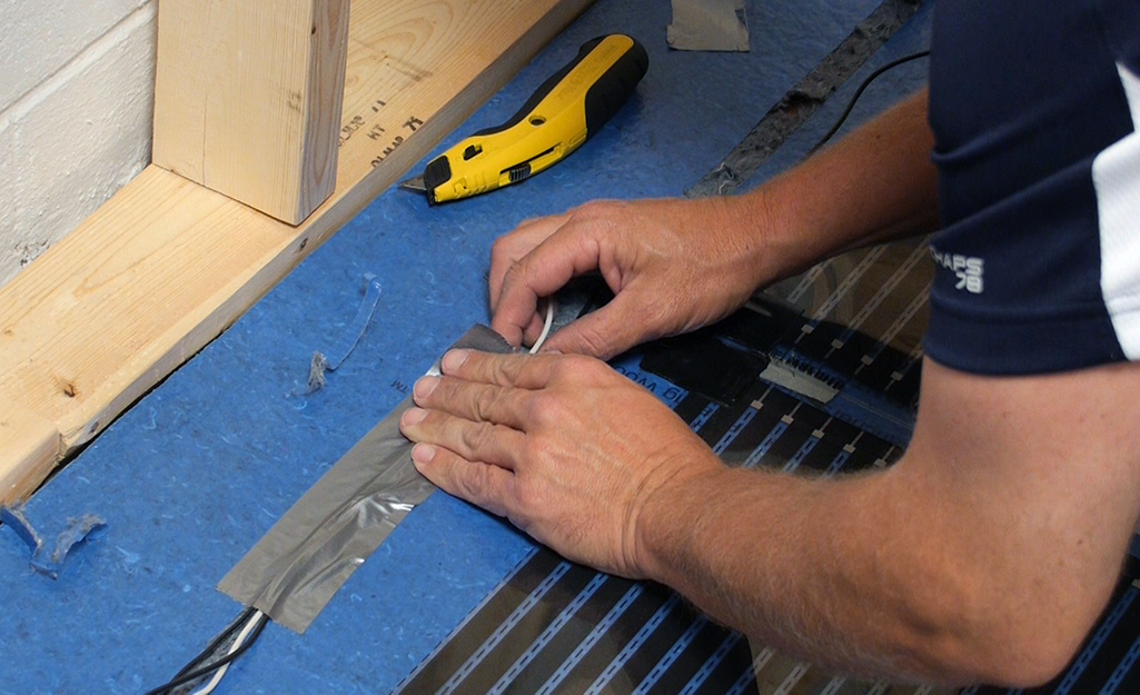 A person uses tape to secure the wires of a radiant heat floor mat.