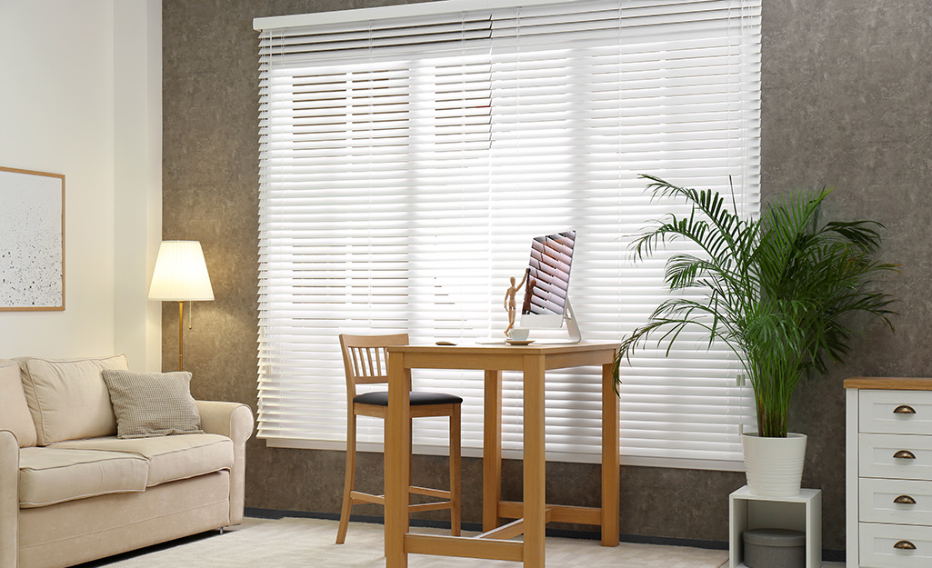 Outside mount horizontal blinds cover the windows in a small living room.