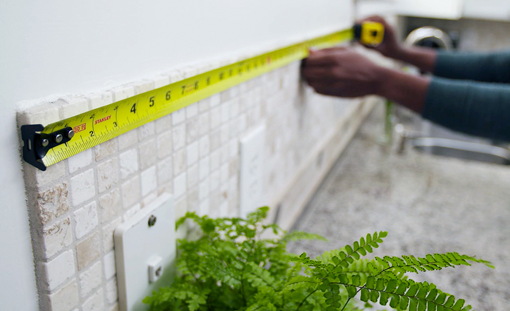 Someone measuring a wall behind a kitchen counter.