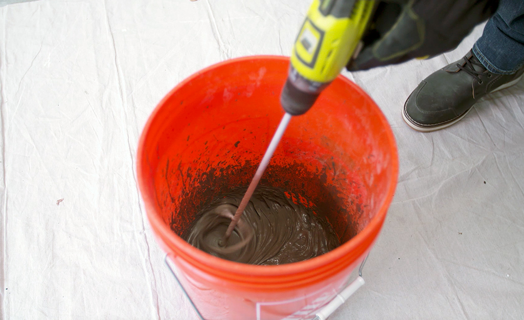 A person pouring water into an orange bucket.