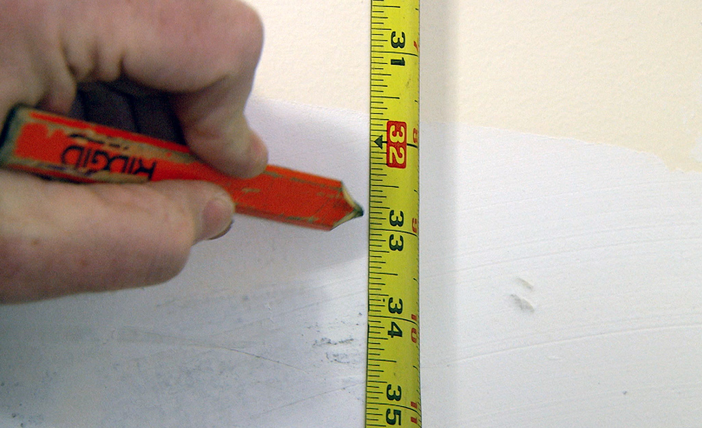 A person marking the location for wall cabinets.