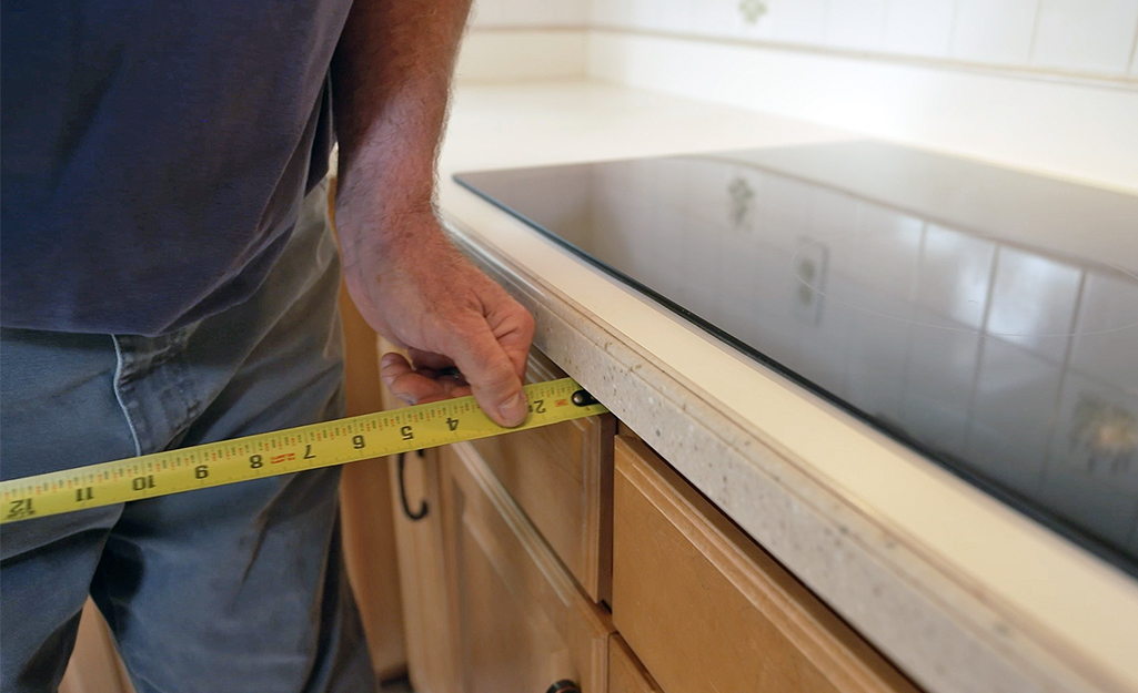 A man uses a tape measure to measure a countertop.