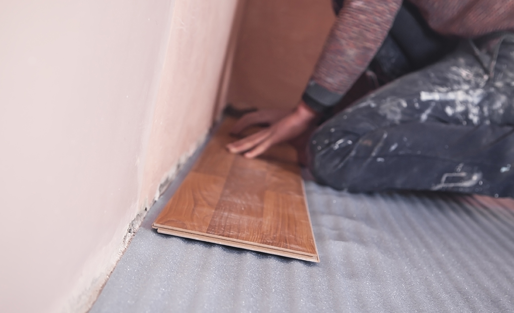 A person lays down the first row of new flooring.