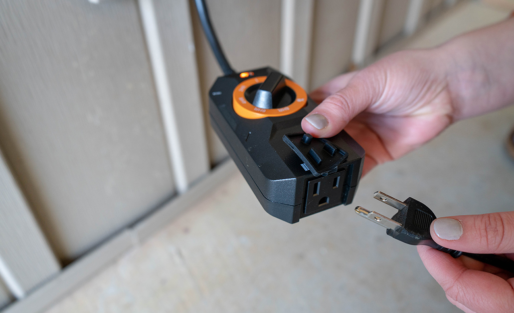 A person plugging in low voltage landscape lights to a transformer with a timer.