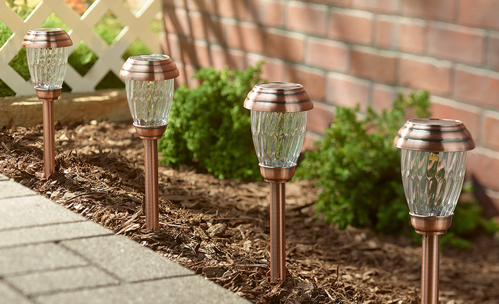 Copper-colored solar landscape lighting installed in a garden bed next to a pathway.