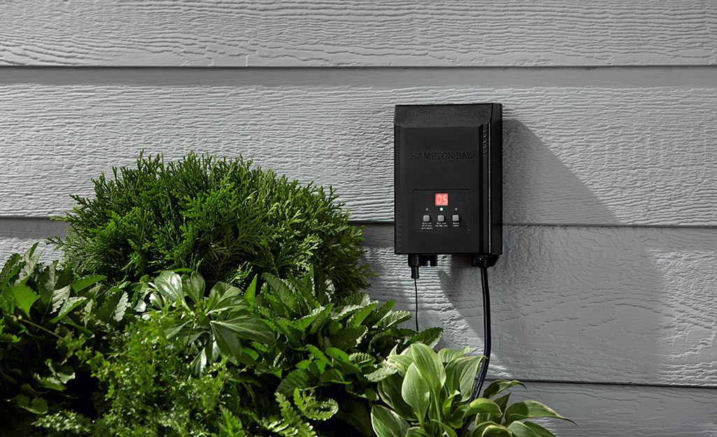 A low voltage landscape lighting transformer mounted to the side of a house.
