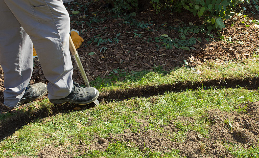 A person digging a narrow trench along a garden bed for the landscape lighting cable.