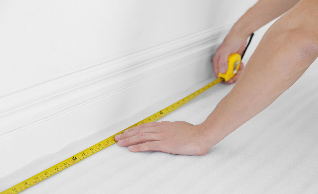 A person measures the length of a floor with a tape measure.