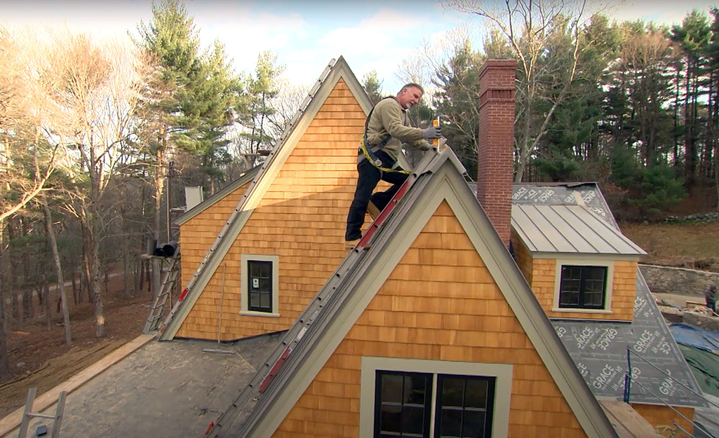 A man wears safety gear to install roofing. 
