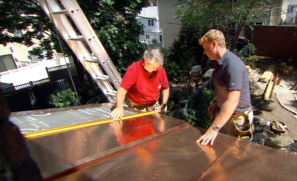 Two people measuring copper roofing panels.