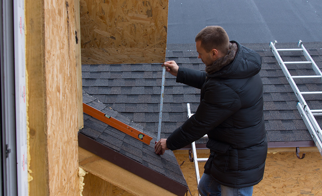 A man wears a winter coat while measuring a roof.