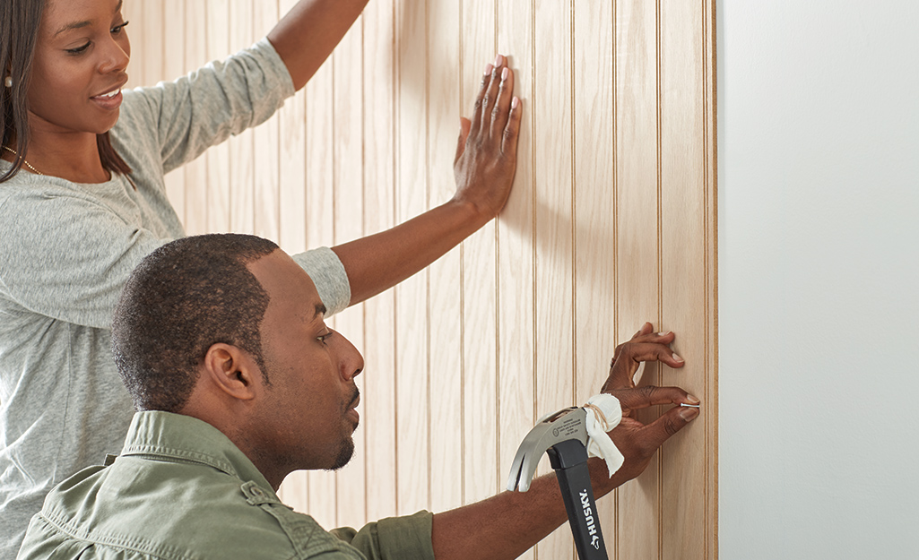 Woman holding paneling while man hammers in finishing nails