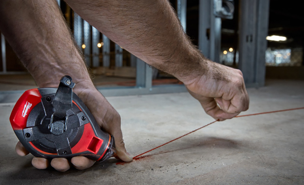 A person using a chalk line to make a mark on a floor before installing parquet tile.