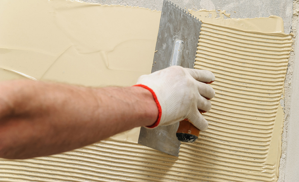 A person creating grooves in a spread of wood adhesive on a floor.