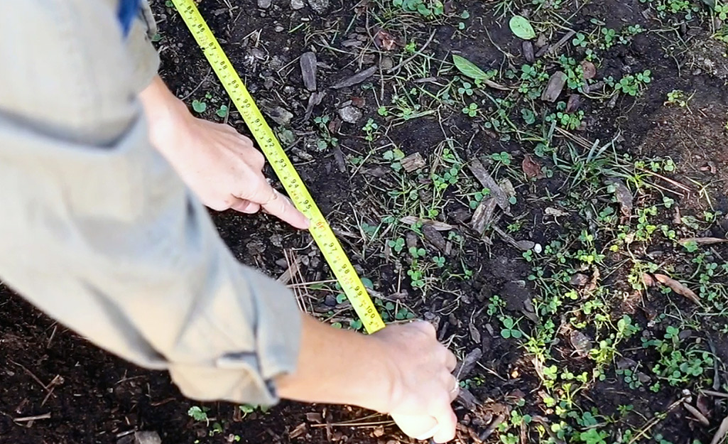 A person uses a measuring tape to measure placement for patio pavers.