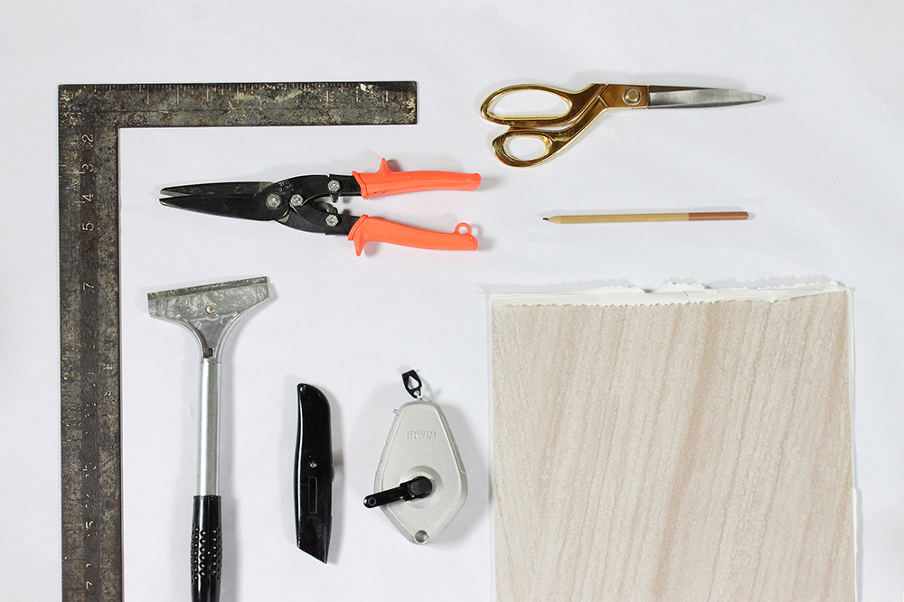 Various tools and materials needed to install peel and stick tile flooring.