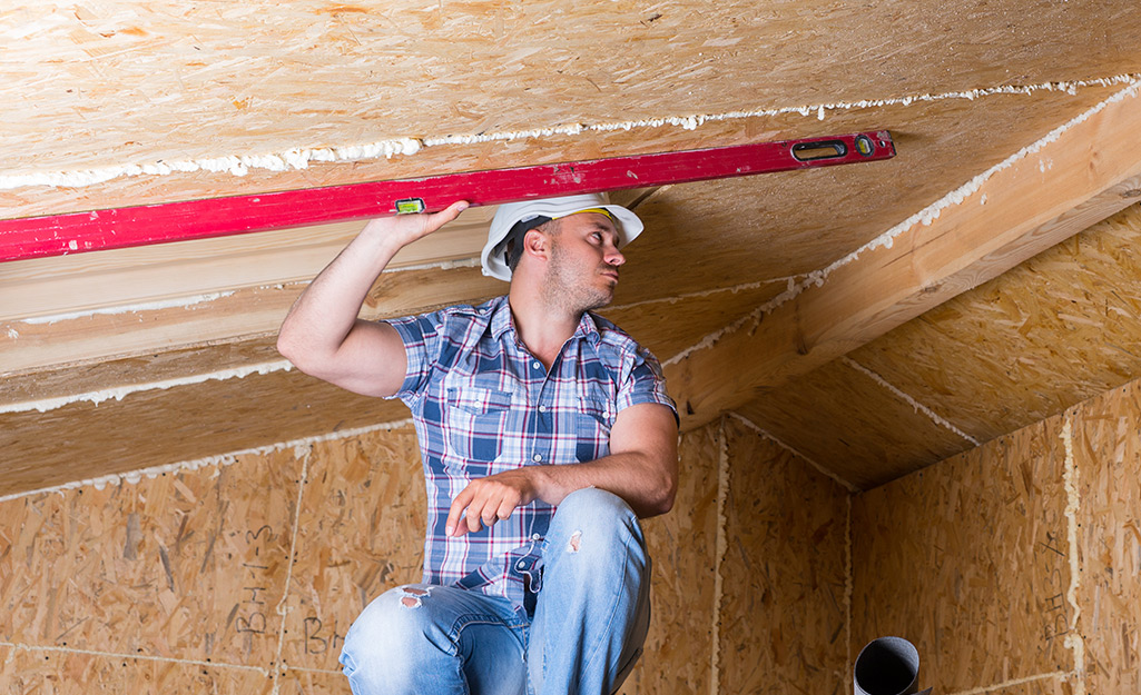 A person takes the measurement of a sloped ceiling. A person takes the measurement of a sloped ceiling.
