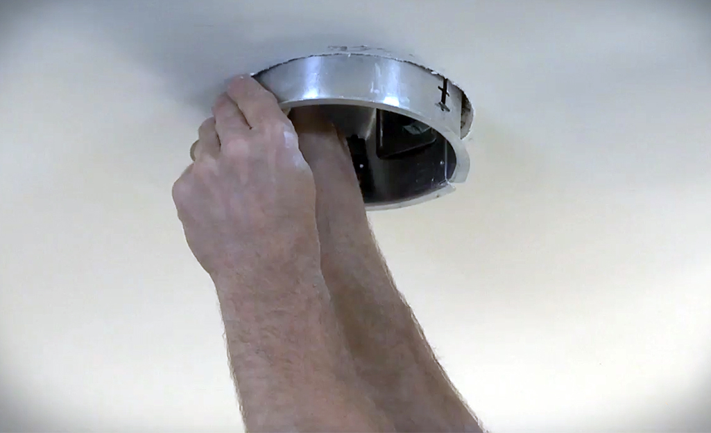 A person pressing the recessed light housing into the hole in the ceiling.