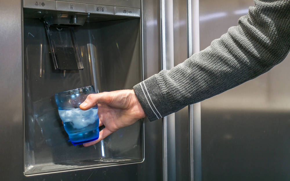 A person fills a cup with water from a refrigerator water dispenser.