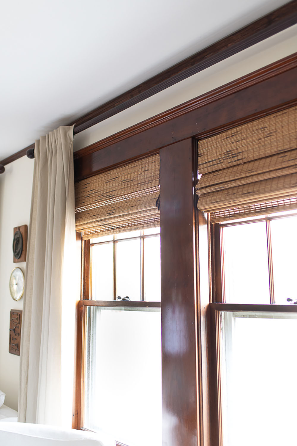 A pair of woven roman shades on windows with dark woodwork.