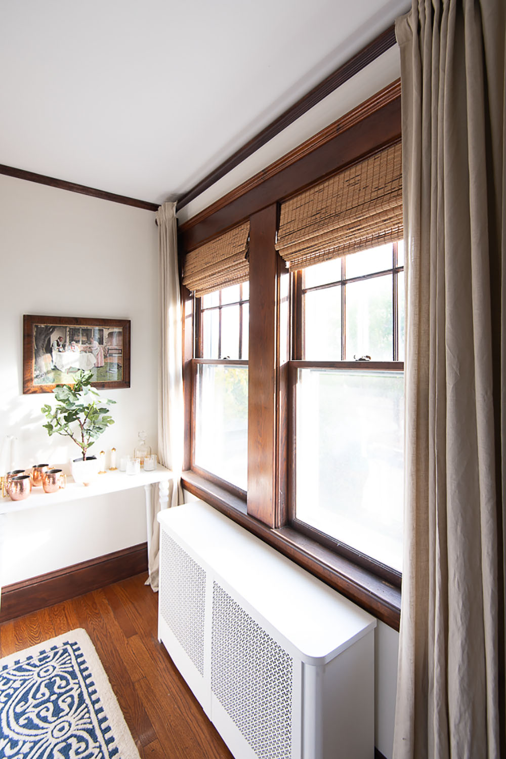 The side view of a window with dark woodwork, curtains, and woven roman shades.