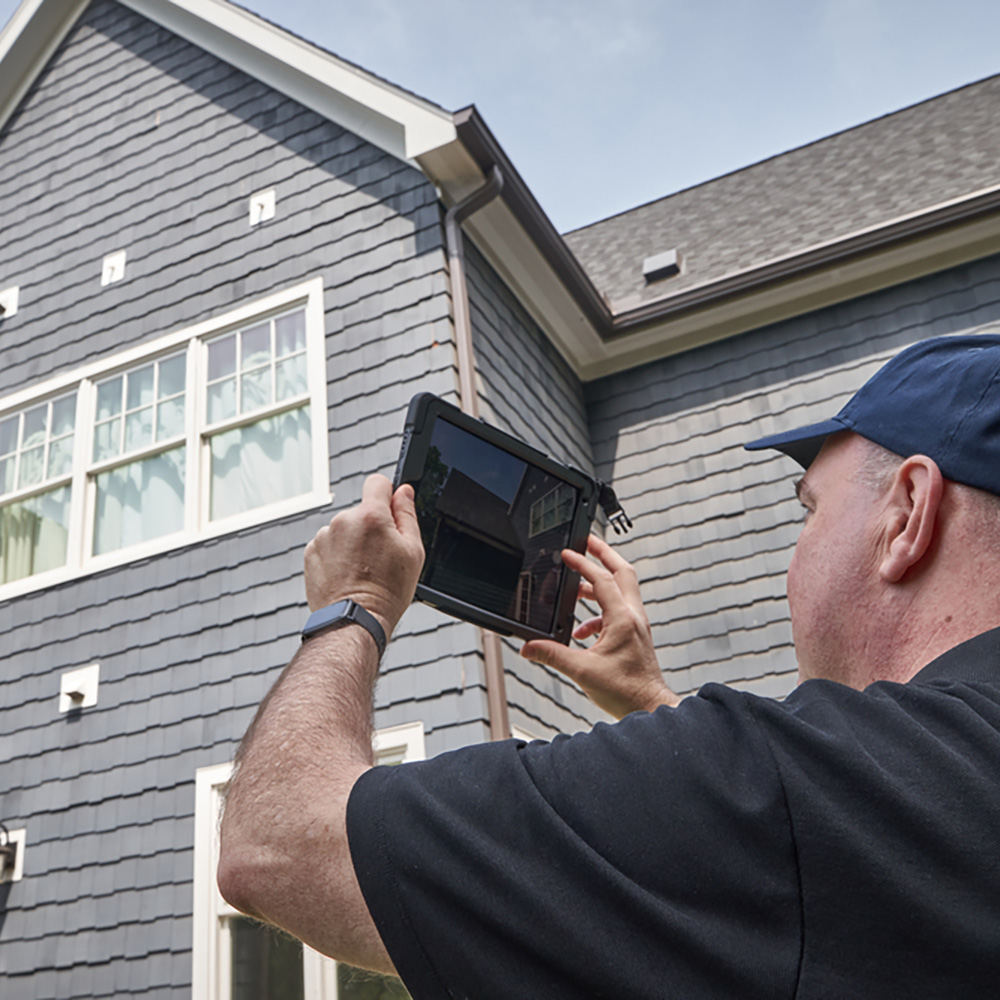 A man analyzing a home with a shingle roof. 