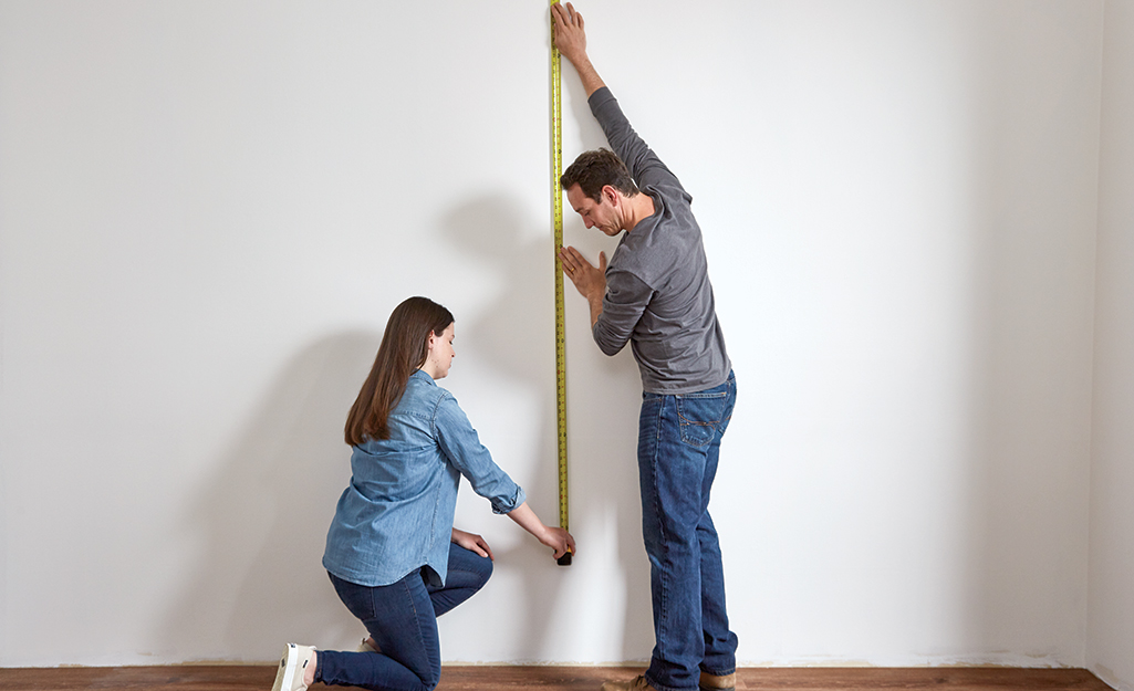 Couple using a tape measure to measure a wall.