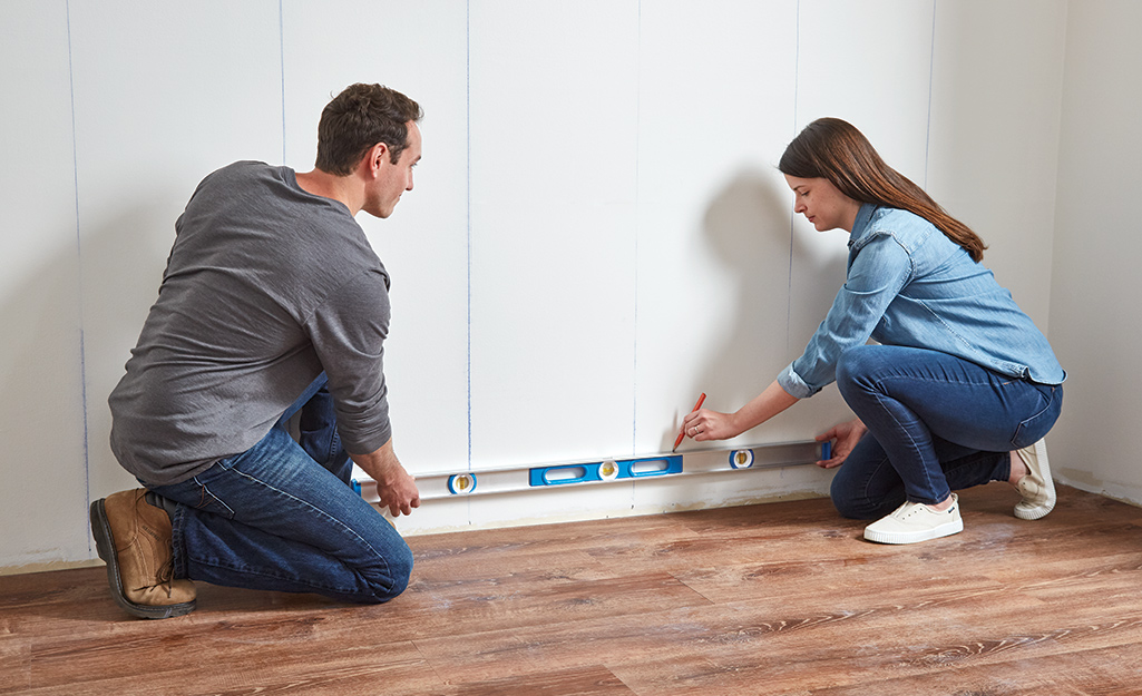 Couple marking a straight horizontal line using a level.